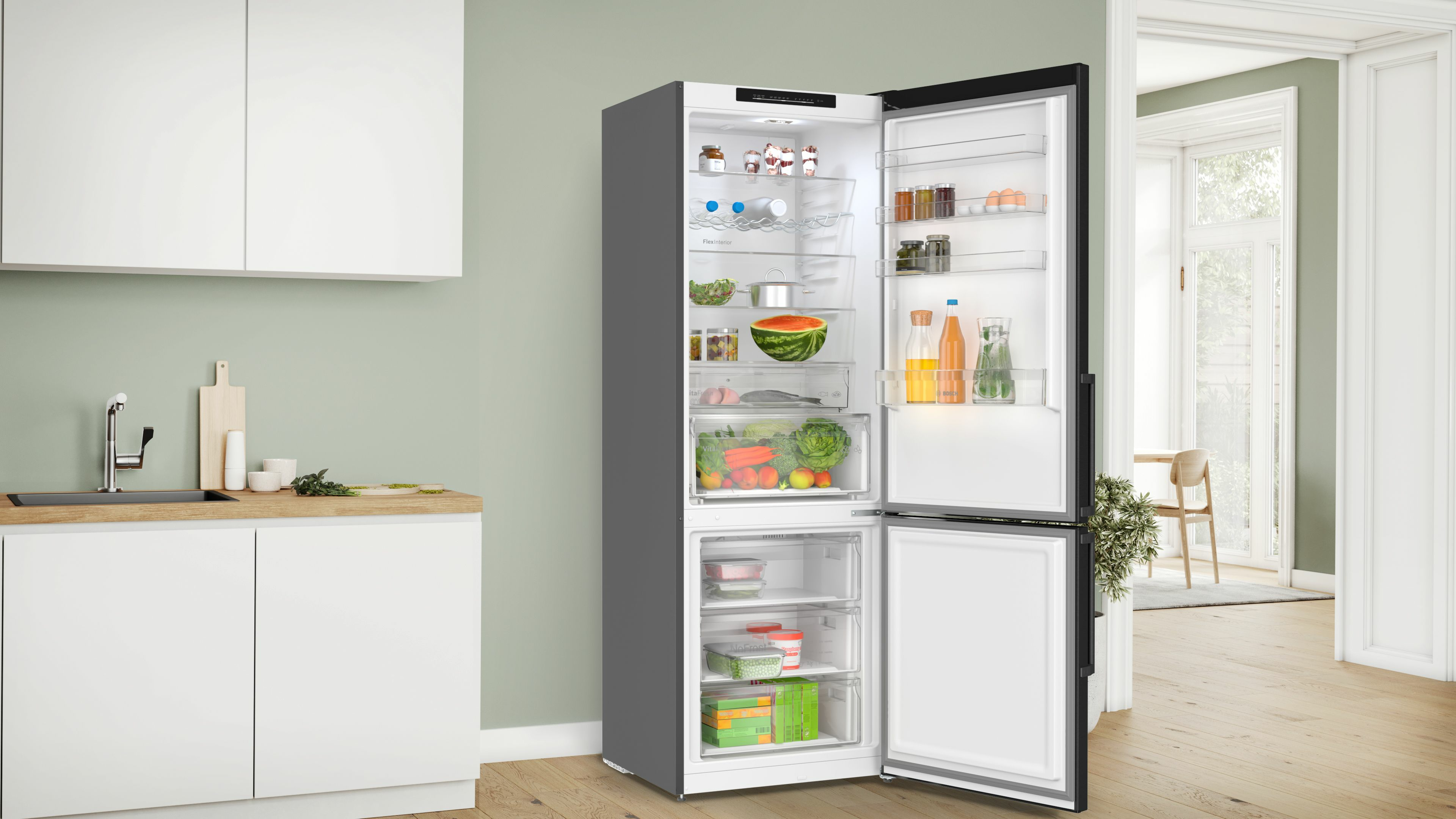Kühlschrank in der Küche, offen, gefüllt mit Lebensmitteln. Küche hat weiße Schränke und Holz-Arbeitsplatte.