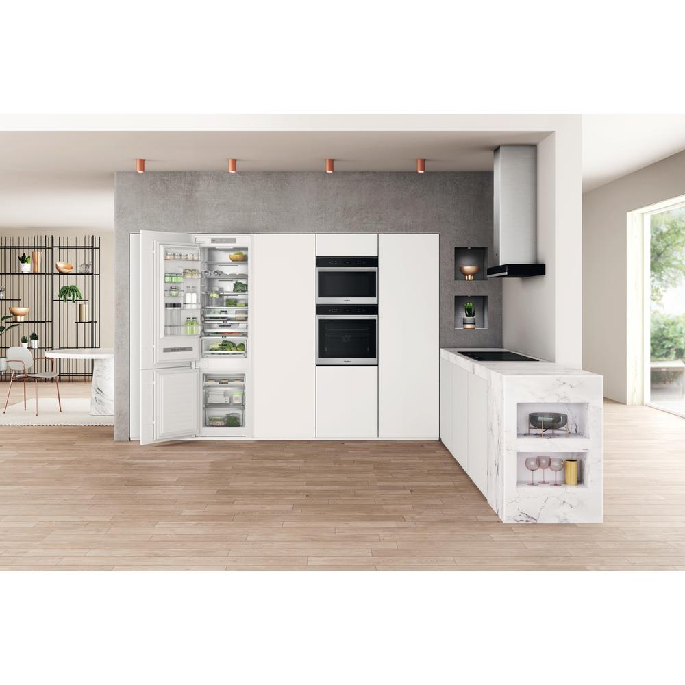 Cucina moderna con mobili bianchi, frigorifero aperto con cibo, forno e piano di lavoro in marmo.