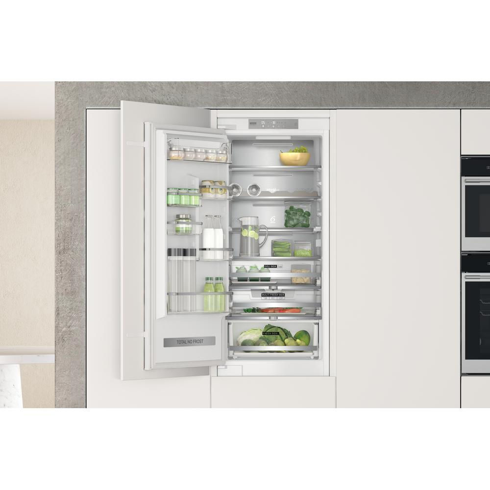 Frigorifero bianco con porta aperta, pieno di generi alimentari. La cucina è bianca.