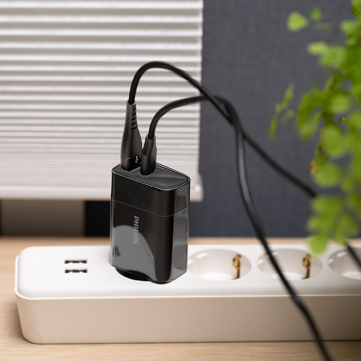 Zwarte Philips-oplader met twee kabels aangesloten op een witte stekkerdoos met twee USB-poorten.