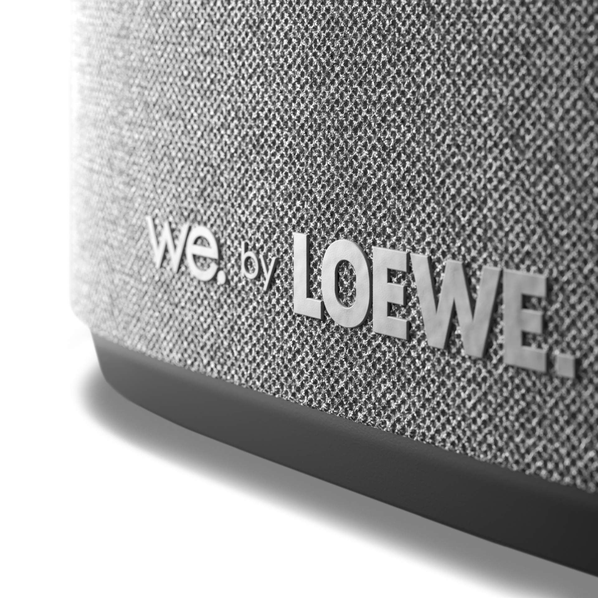 Nahaufnahme eines Lautsprechers mit grauem Stoffbezug und dem Text "we. by LOEWE."