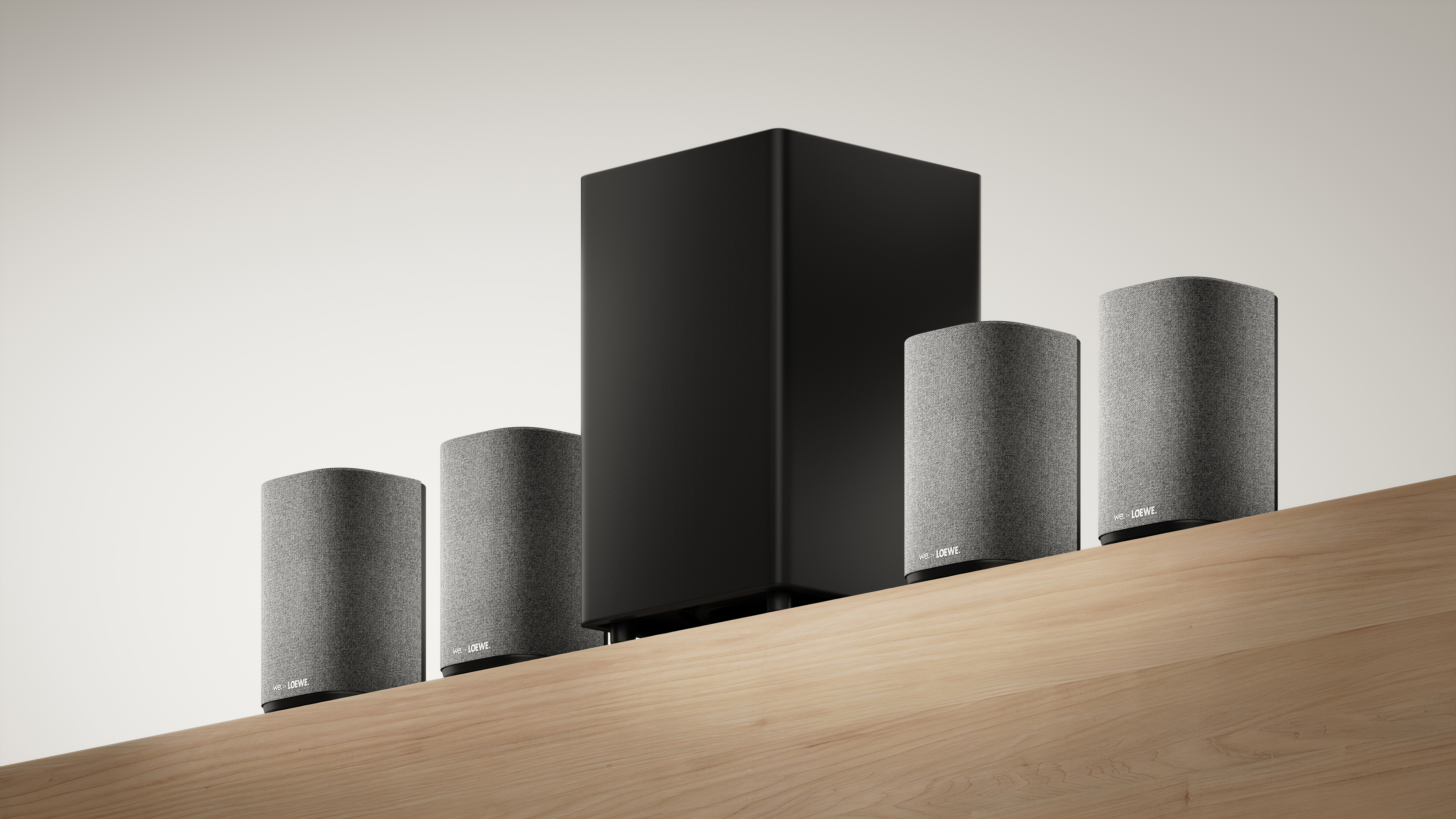 Ein Loewe-Soundsystem mit Subwoofer und fünf Lautsprechern auf einer Holzoberfläche vor weißem Hintergrund.
