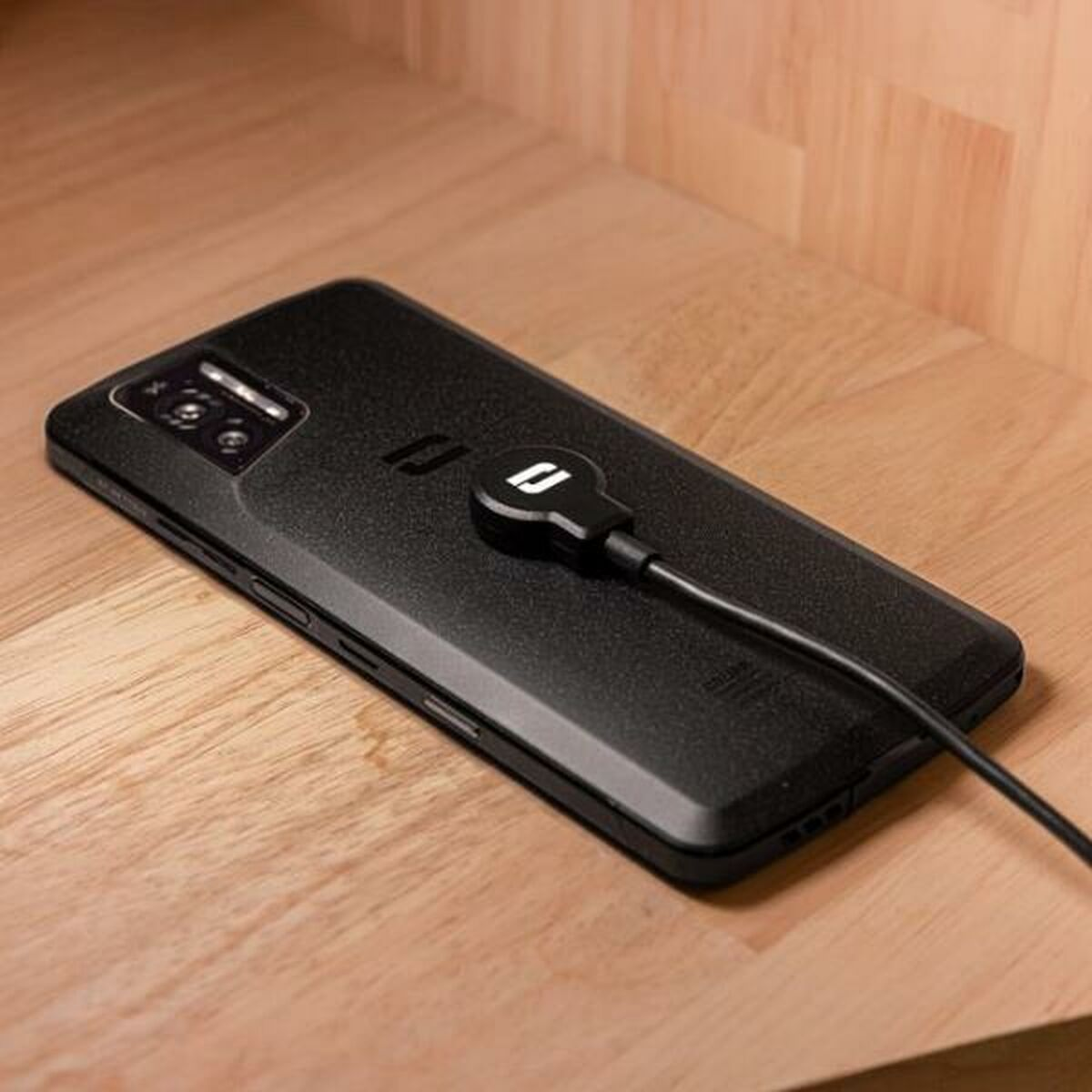 Telefono nero con cavo di ricarica su superficie in legno.