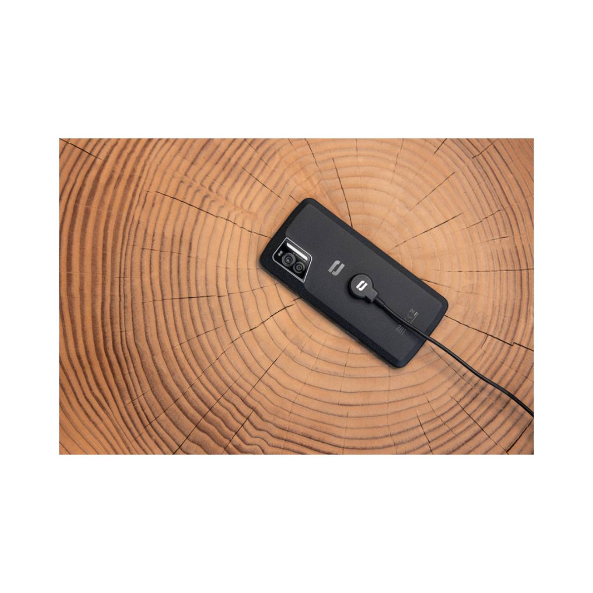 Telefono nero con cavo di ricarica collegato, su una superficie di legno.