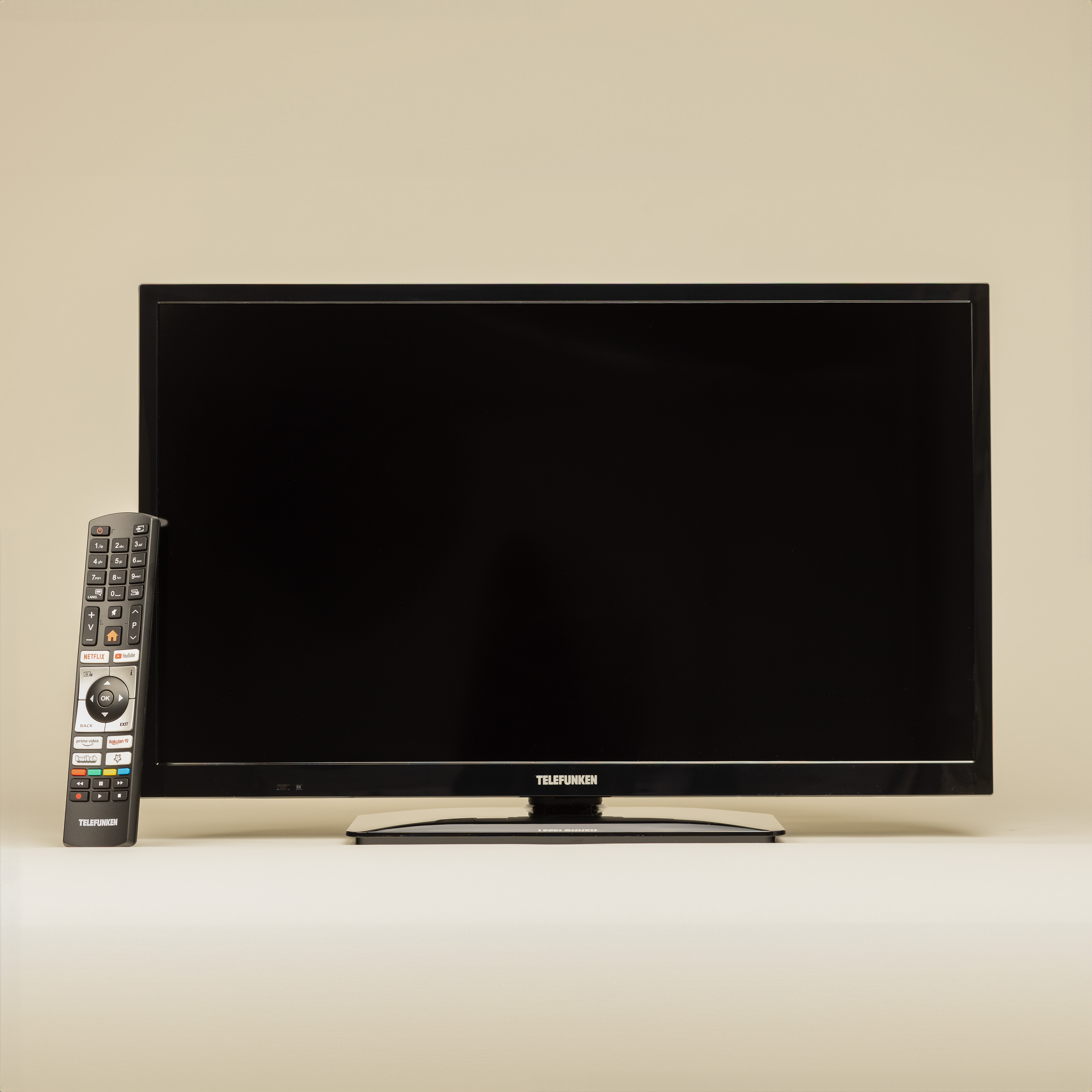 Schwarzer Telefunken-Fernseher mit Fernbedienung vor hellbeigem Hintergrund.