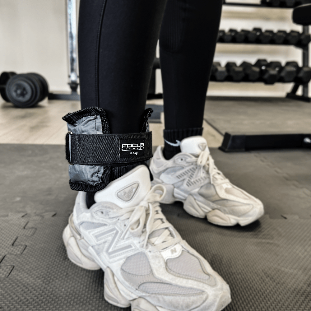 Persoon met zwarte leggings en witte sneakers met Focus Fitness enkelgewichten.