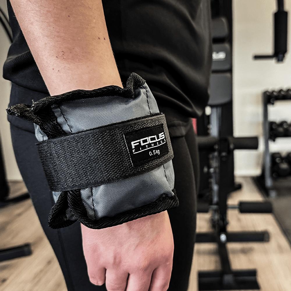 Persoon met zwarte enkelgewicht. Focus Fitness merk, 0,5 kg label zichtbaar.