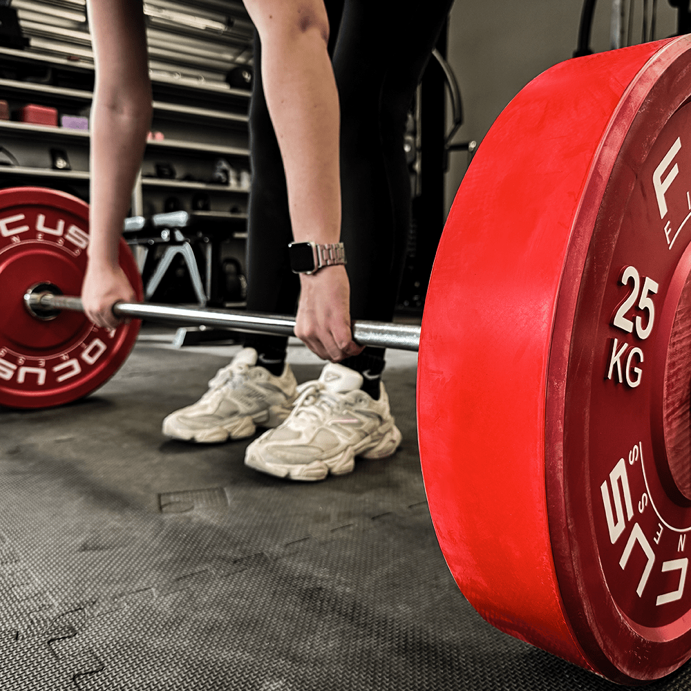 Persoon die barbell tilt met rode gewichten in een sportschool.