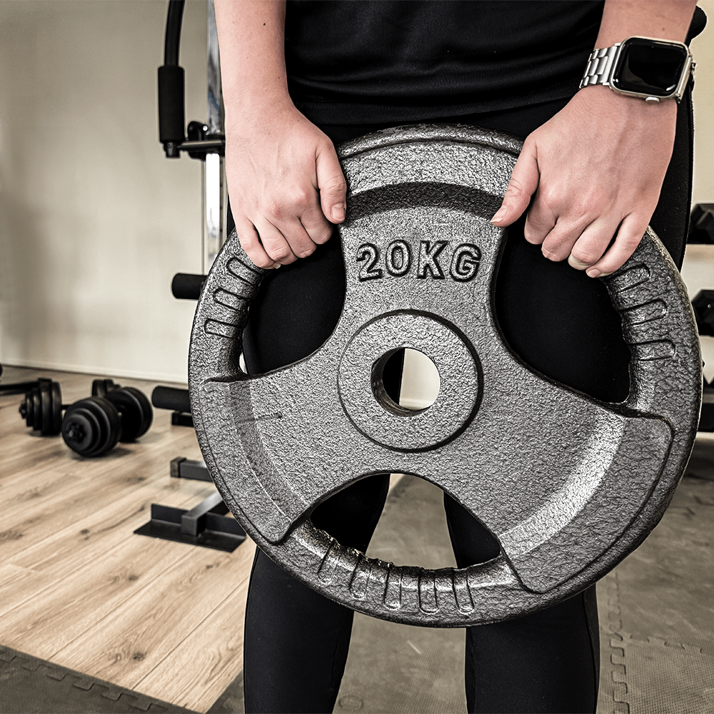 Een persoon houdt een 20KG gewichtsschijf vast. Fitnessapparatuur op de achtergrond.