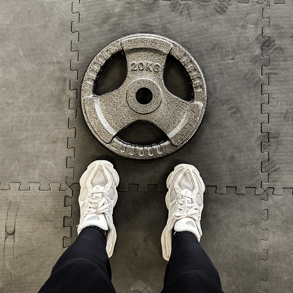 Voeten van een persoon in witte sneakers, staand voor een gewicht van 20 kg.
