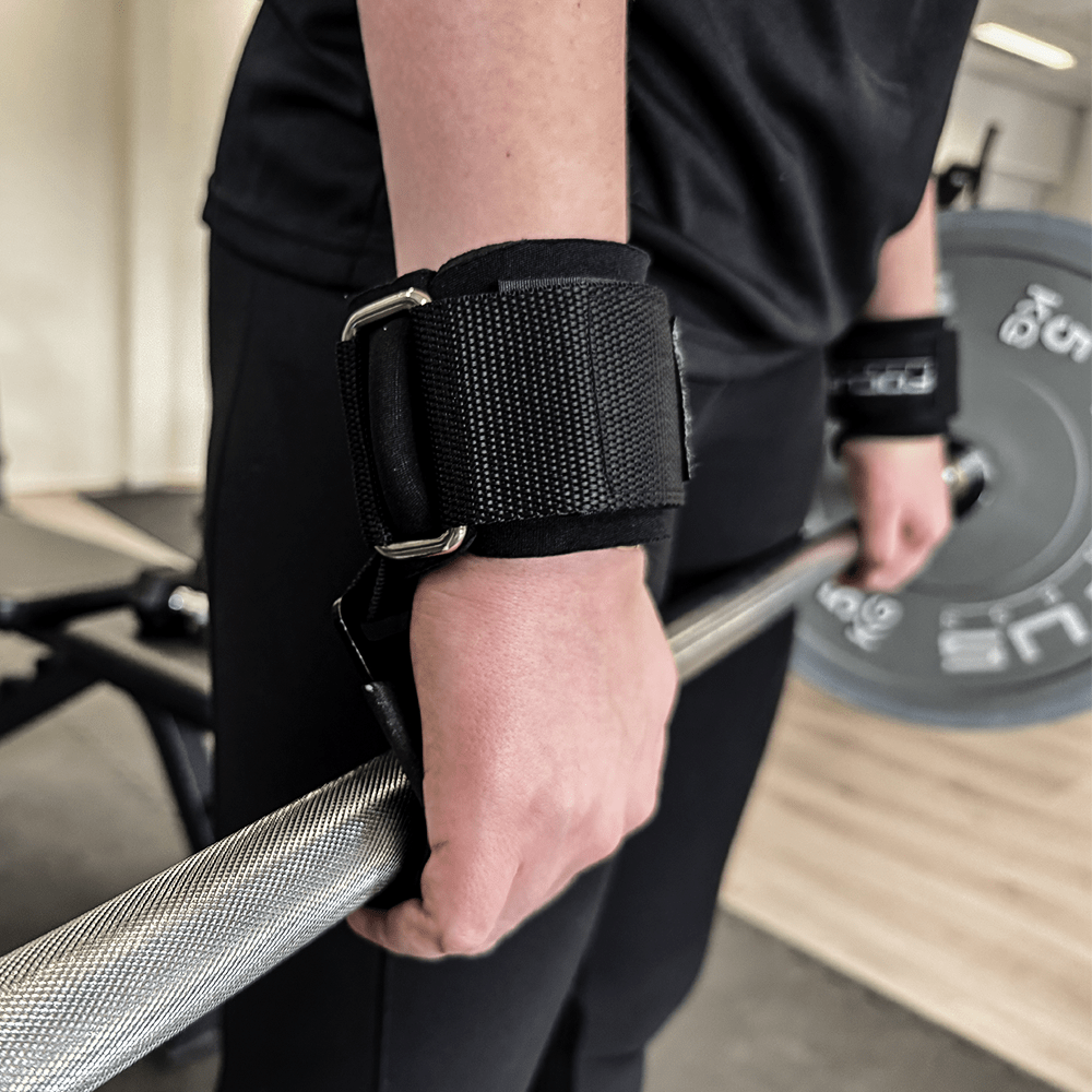 Persoon met zwarte polsbanden die een barbell vasthoudt in een sportschool.