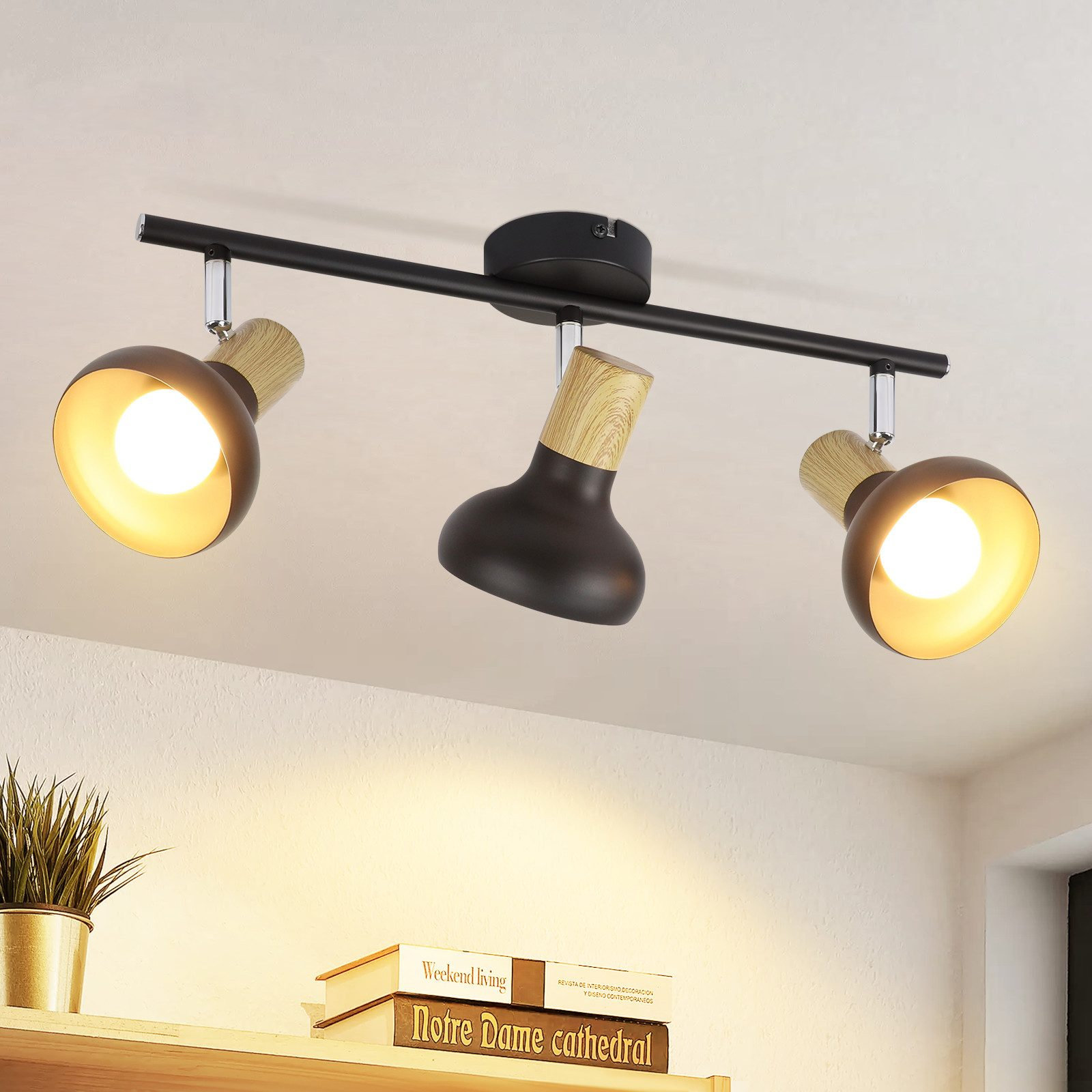 Trzy reflektory na czarnym drążku, zamontowane na białym suficie, książki poniżej.