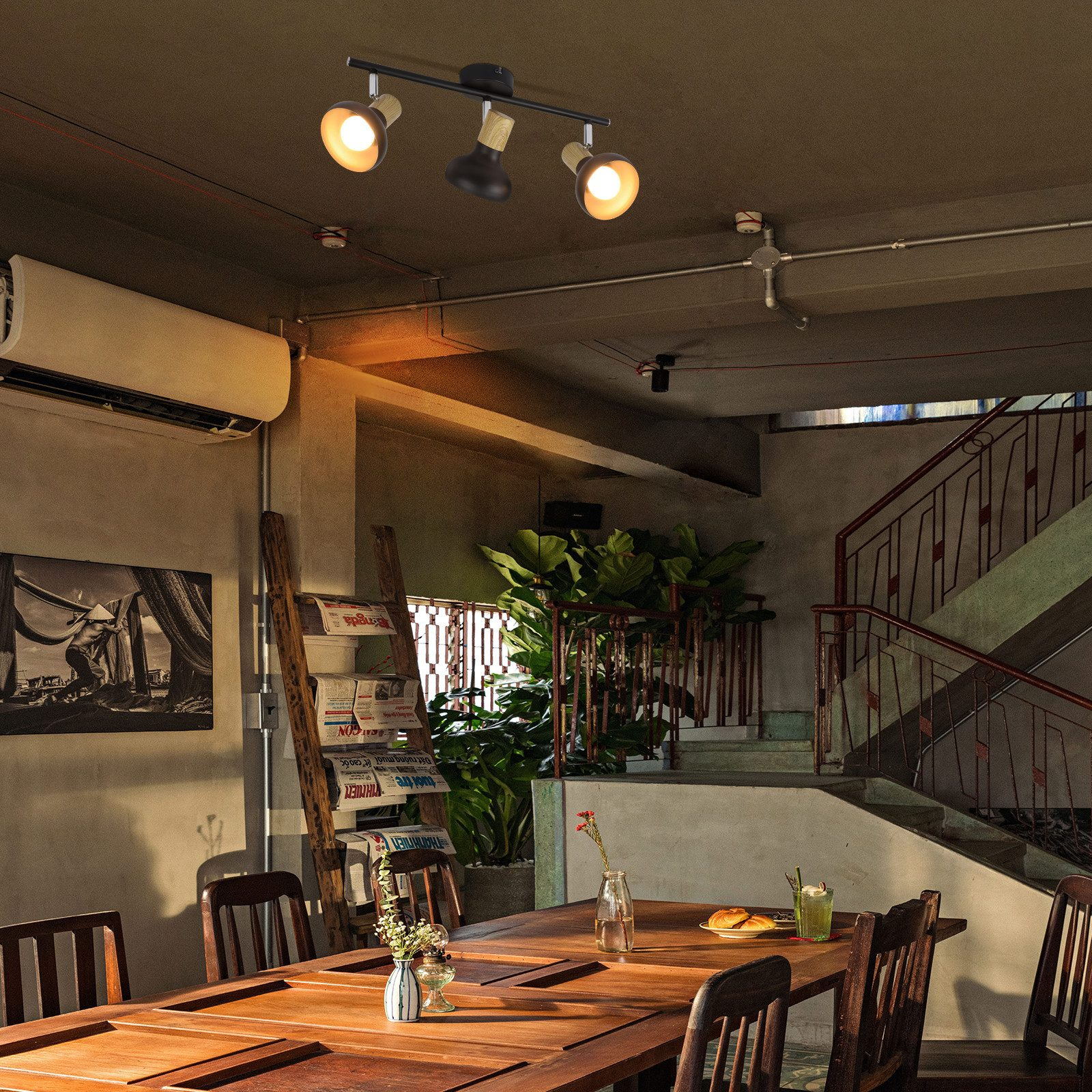 Sufit z reflektorami. Drewniany stół z krzesłami. Schody w tle. Klimatyzator na ścianie.