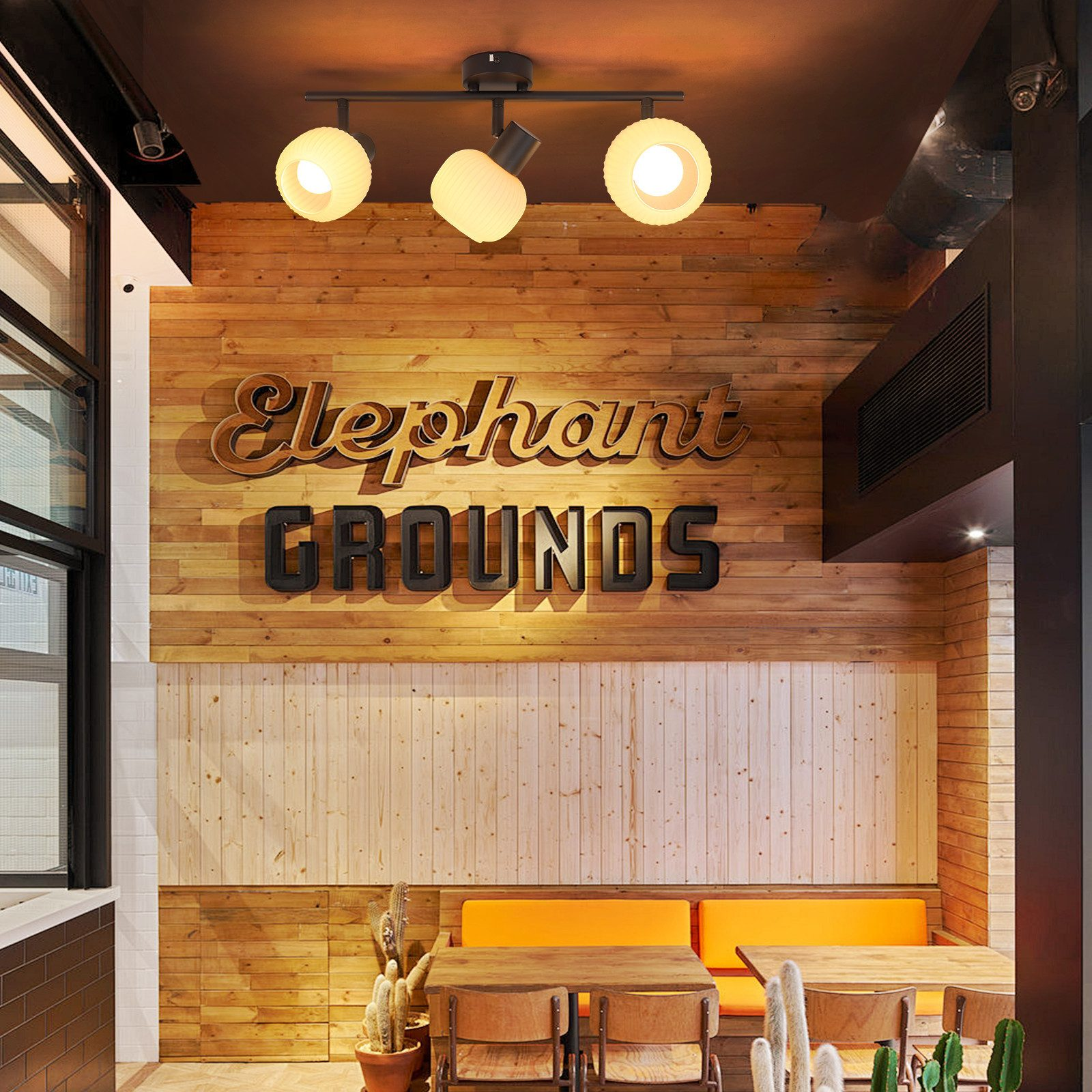 Wnętrze kawiarni z drewnianymi ścianami i pomarańczowymi siedzeniami, z dekoracyjnym światłem.