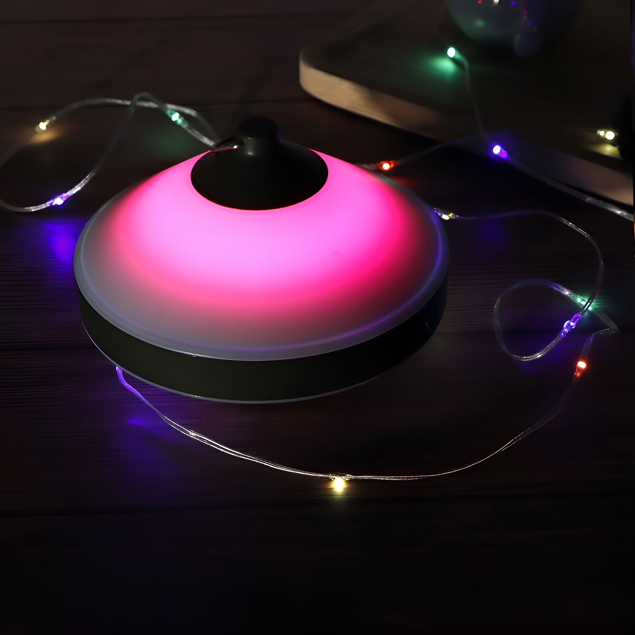 Eine runde, dunkelgrüne Lampe, die rosa Licht ausstrahlt, mit einer Schnur bunter Lichter drumherum.