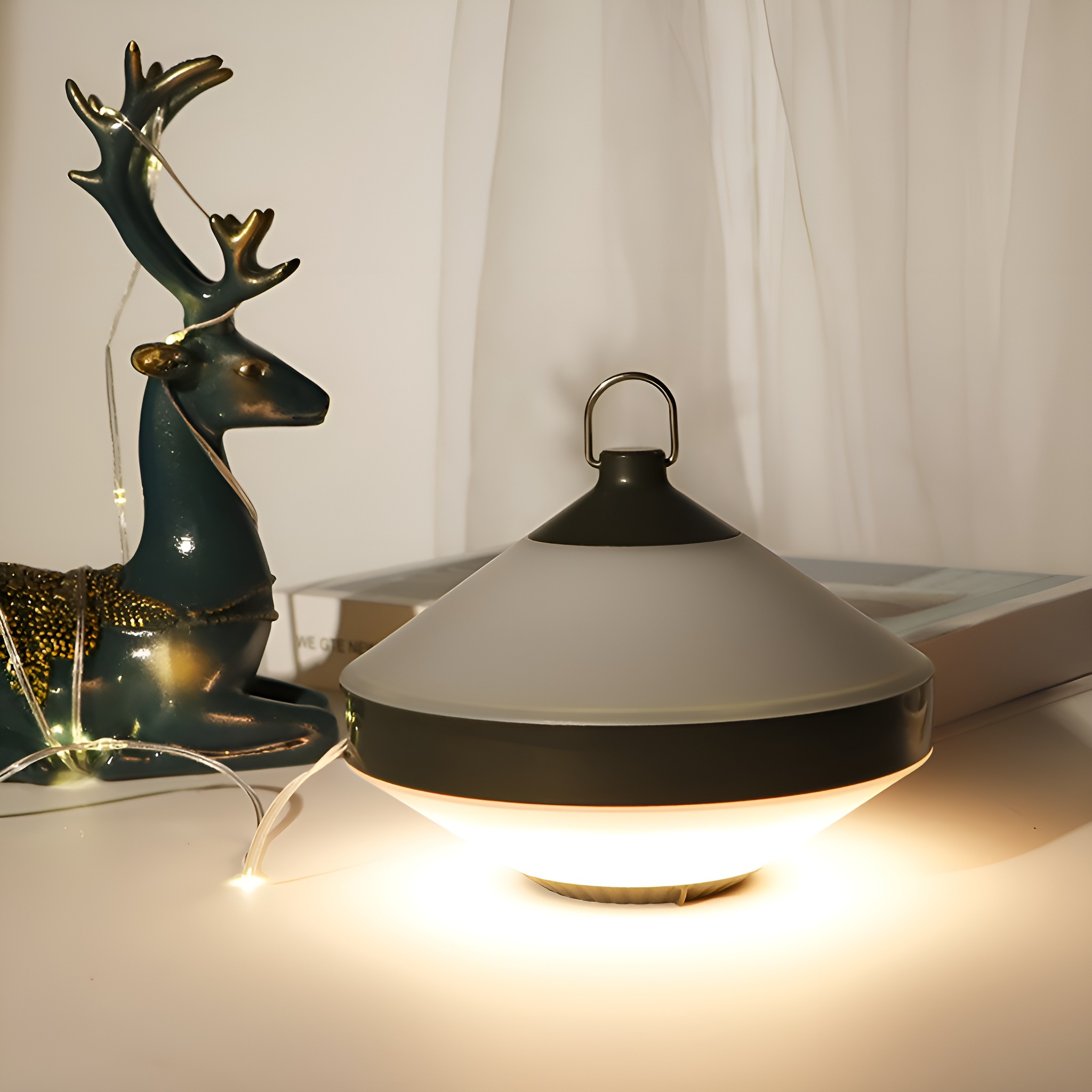 Eine beleuchtete Lampe mit Griff, eine Hirschstatue und Lichterketten auf einer weißen Oberfläche.