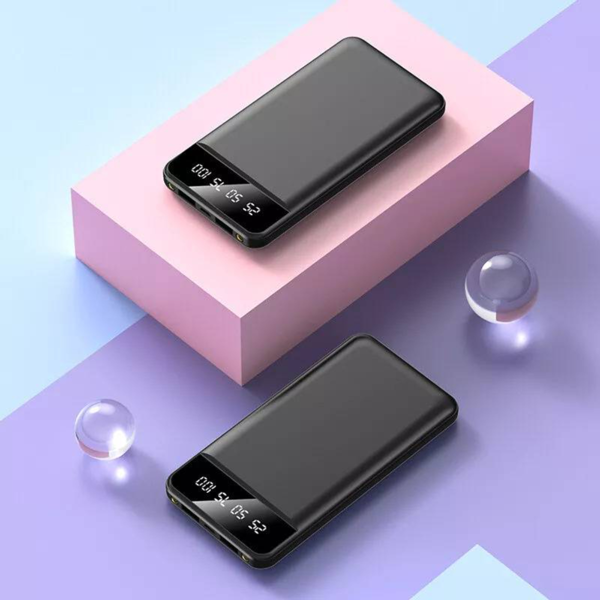 Zwei schwarze Powerbanks auf einer rosa Oberfläche, mit zwei transparenten Kugeln.