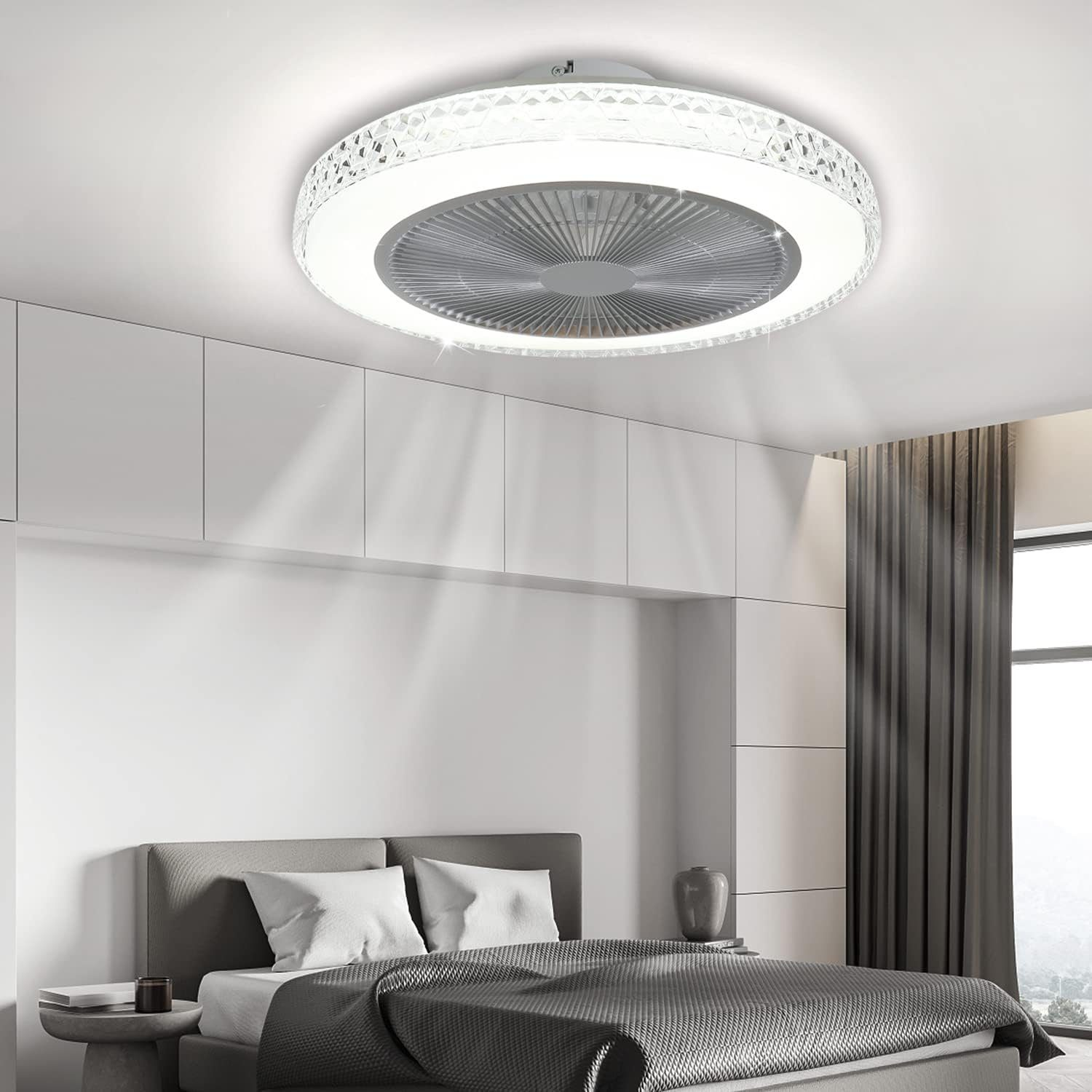 Ventilatore a soffitto con luci in una camera da letto. La ventola è rotonda, bianca e ha un anello luminoso. La stanza ha un letto.