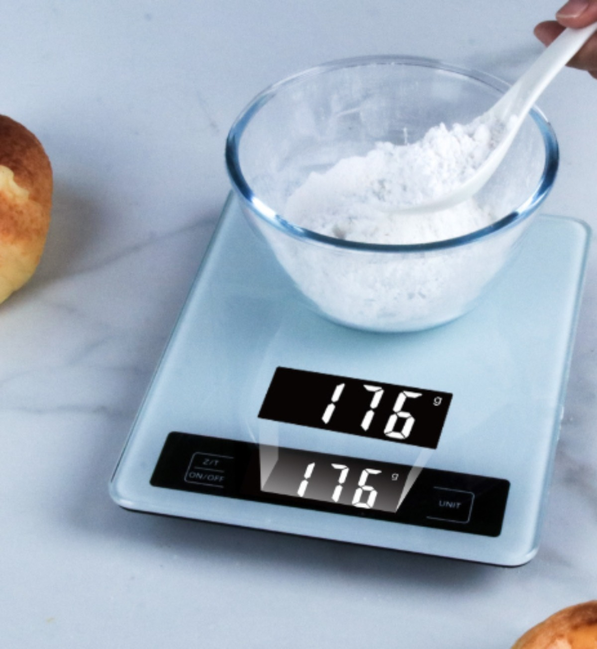 Digitale Küchenwaage mit Mehl, das in einer Glasschüssel abgewogen wird, Löffel in der Hand.