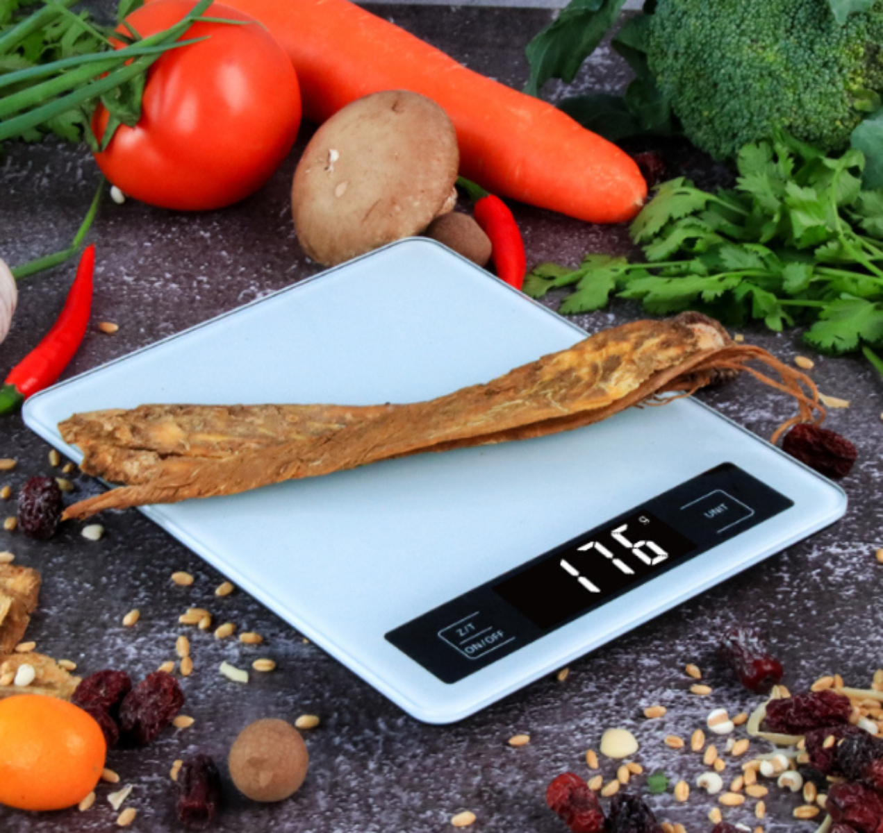 Eine digitale Küchenwaage, die 176 Gramm anzeigt. Gemüse, Obst und Gewürze umgeben die Waage.