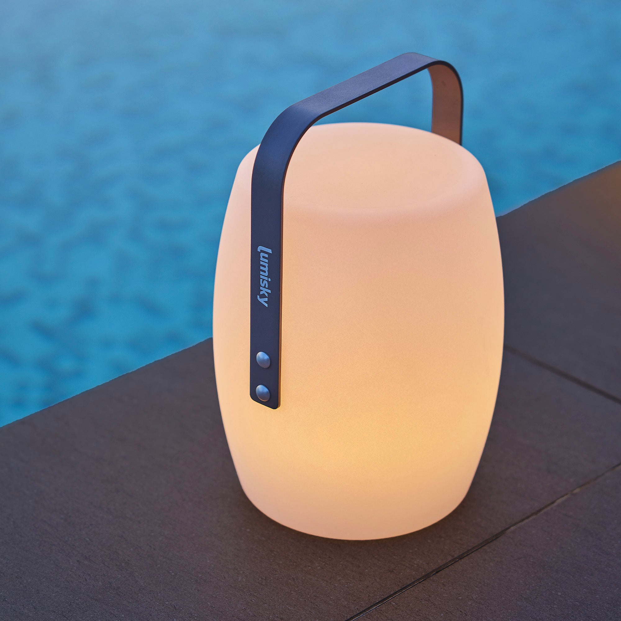 Eine leuchtende weiße Außenlampe mit schwarzem Griff, an einem Pool.