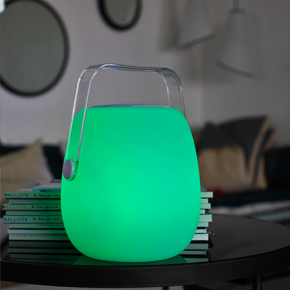 Una lanterna verde brillante con una maniglia, su un tavolo con libri e uno sfondo scuro.
