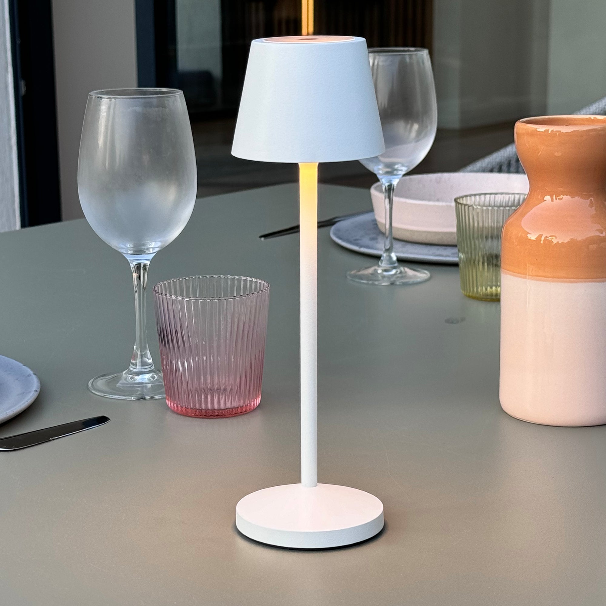 Weiße Tischlampe auf einem Tisch mit Gläsern und einer Vase. Umgebungslicht, minimalistische Umgebung.