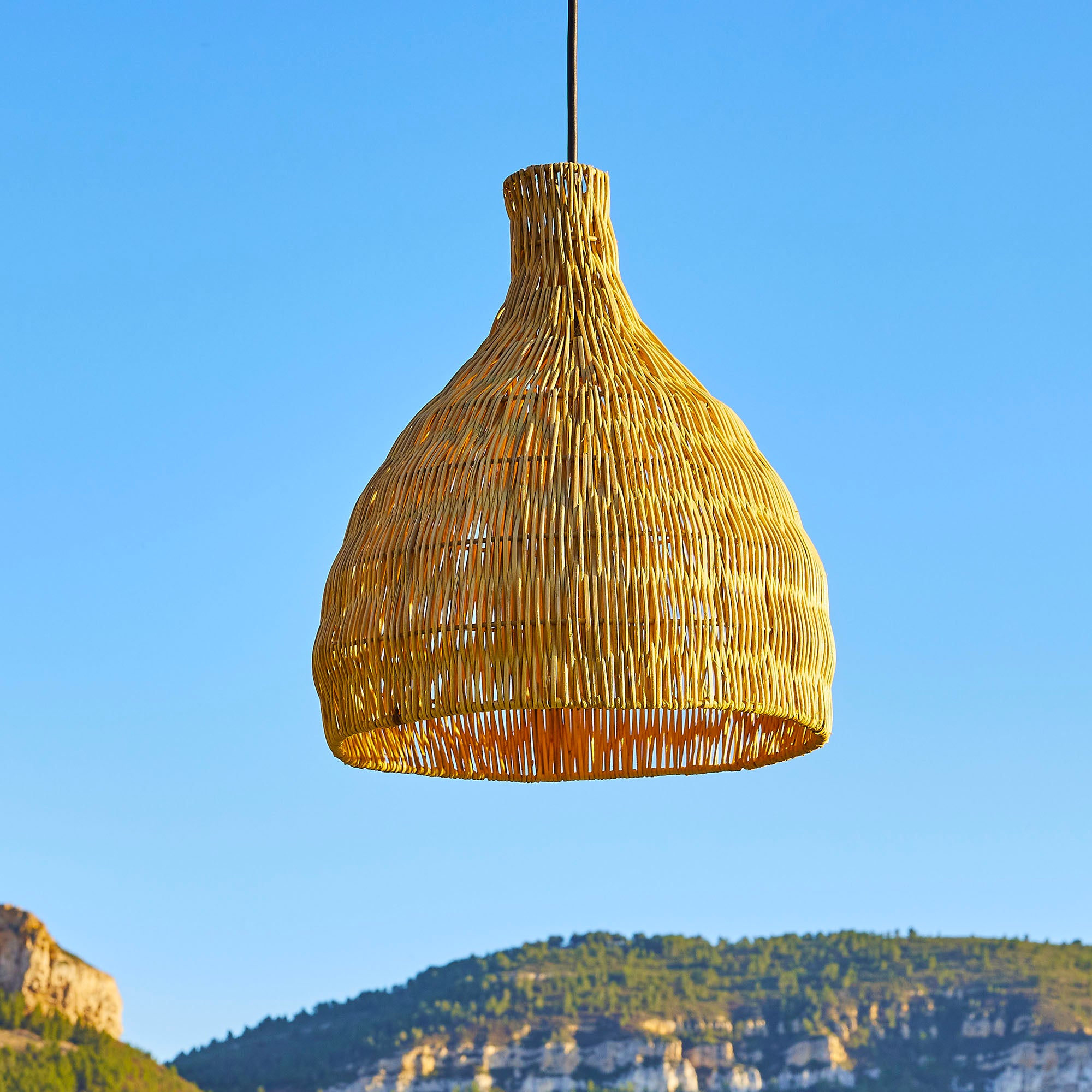 Gewebte beige Lampe vor blauem Himmel und Bergkulisse.