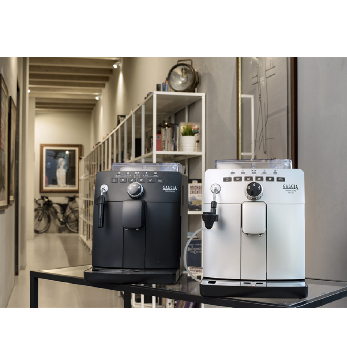 Dwa czarno-białe ekspresy do espresso na szklanym stole, w nowoczesnym, dobrze oświetlonym pokoju.