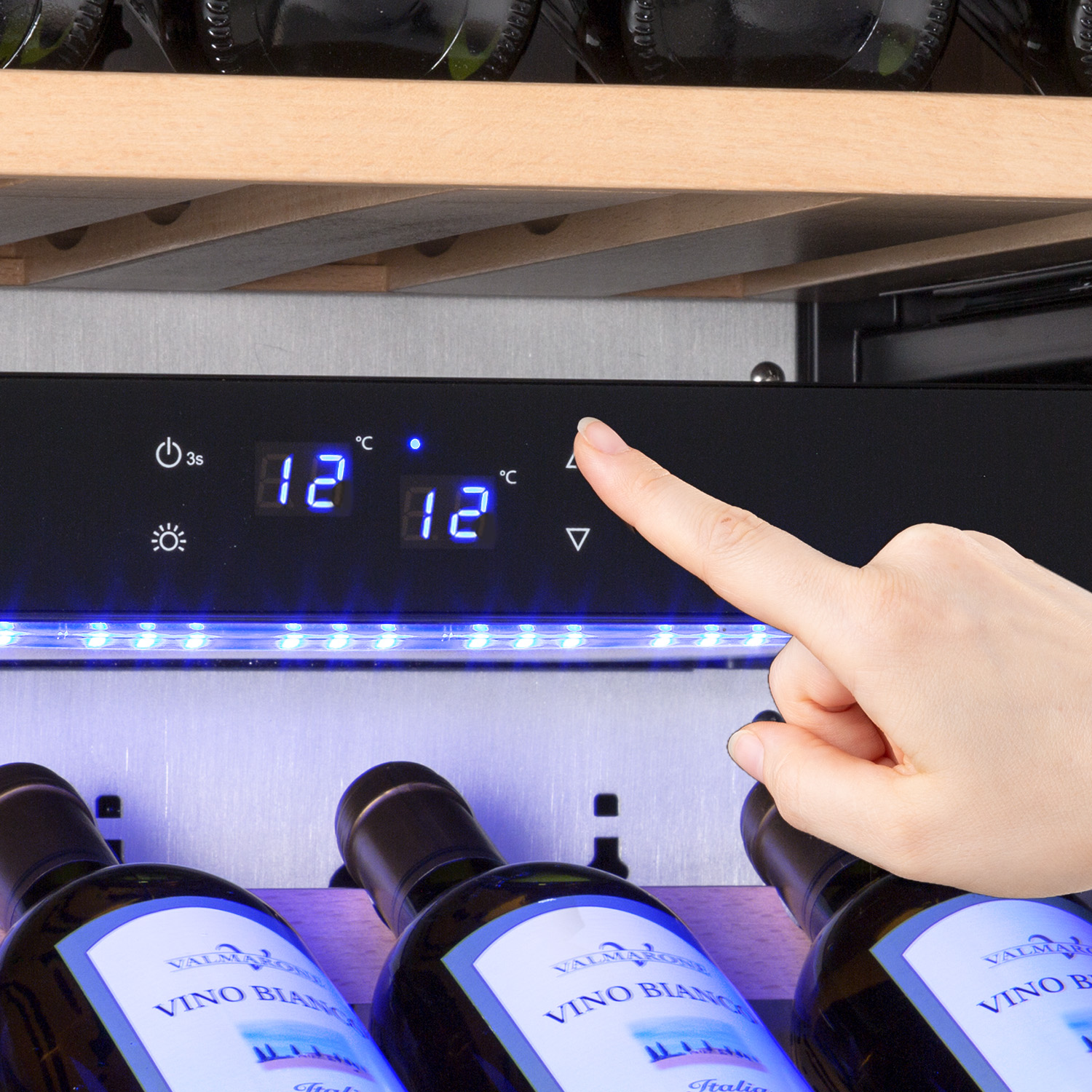 Una mano regola il display digitale di una cantinetta. Ci sono bottiglie di vino nel frigorifero. Il display mostra 12°C.