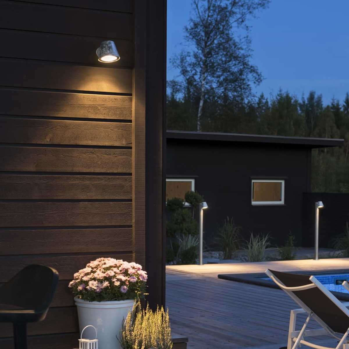 Außenansicht in der Dämmerung. Haus, Pool und Blumen werden von Lichtern beleuchtet. Ein Deckchair befindet sich in der Nähe des Pools.