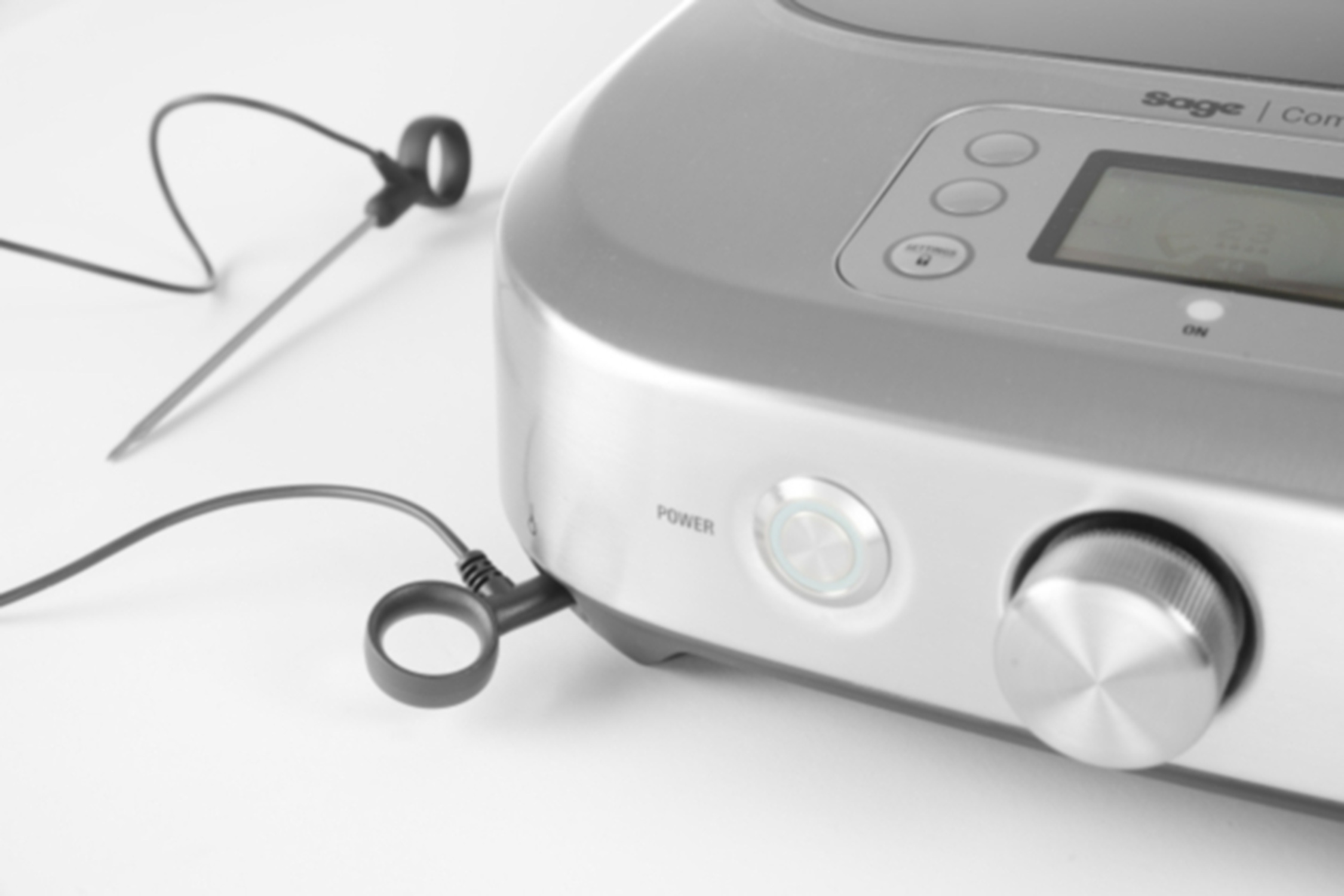 Silver kitchen appliance with power button and dial, probe connected.
