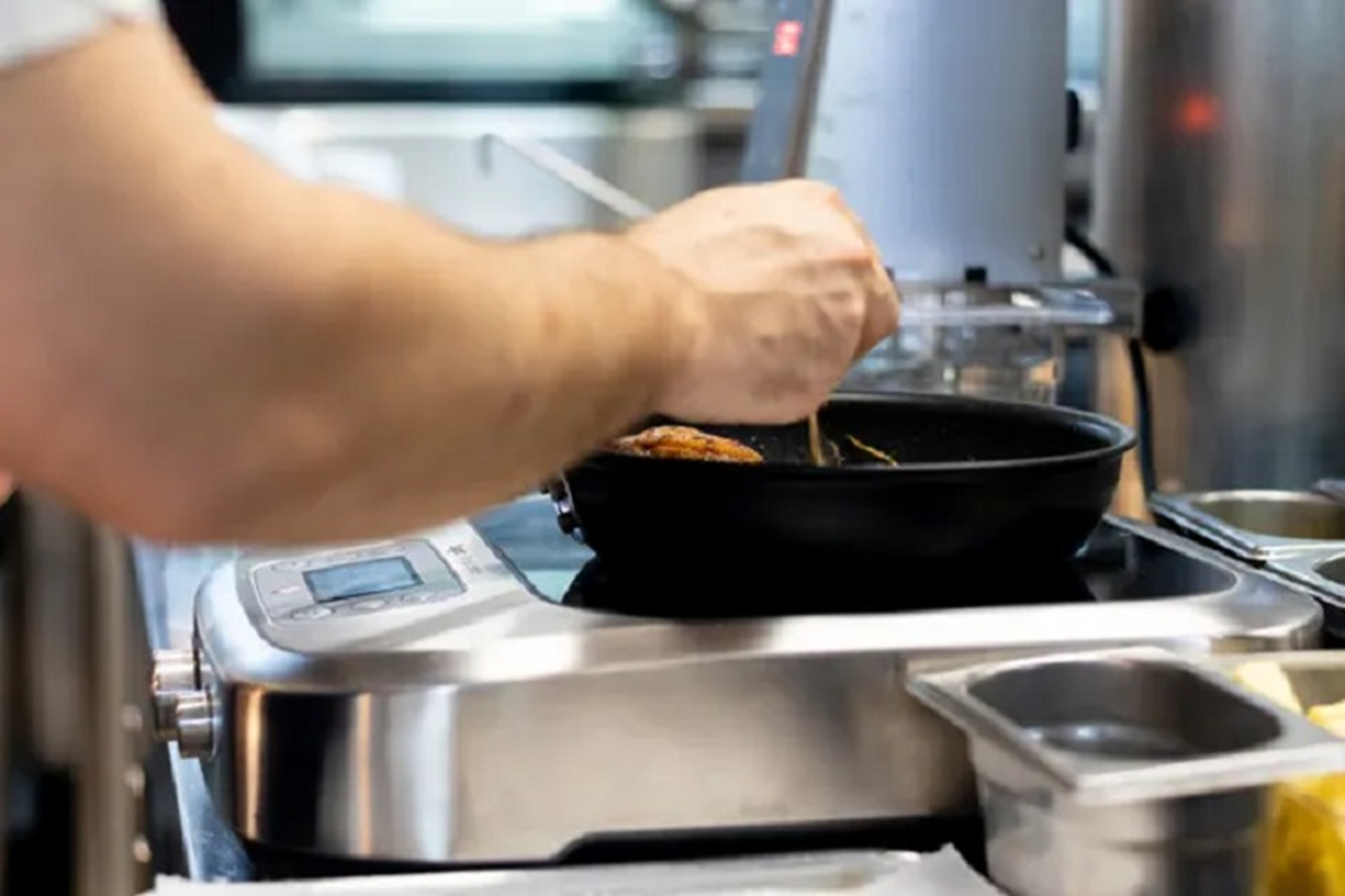 A person cooking food in a pan on a silver induction cooktop.
