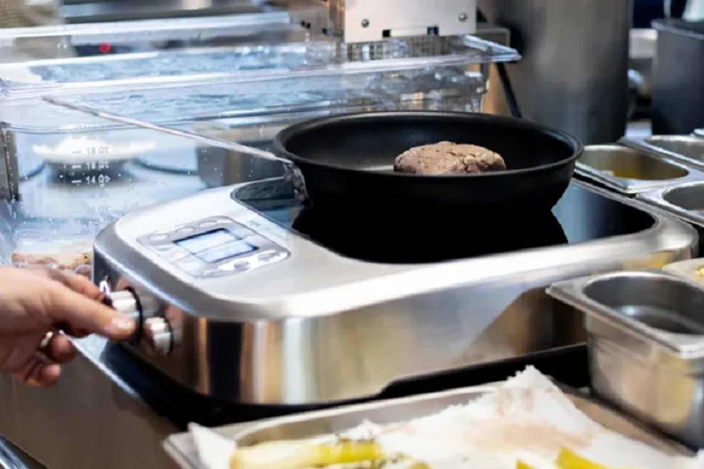 A person cooking in a restaurant, with a burger in a pan on a stove.