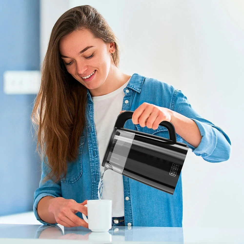 Donna che versa acqua da un bollitore nero in una tazza bianca.