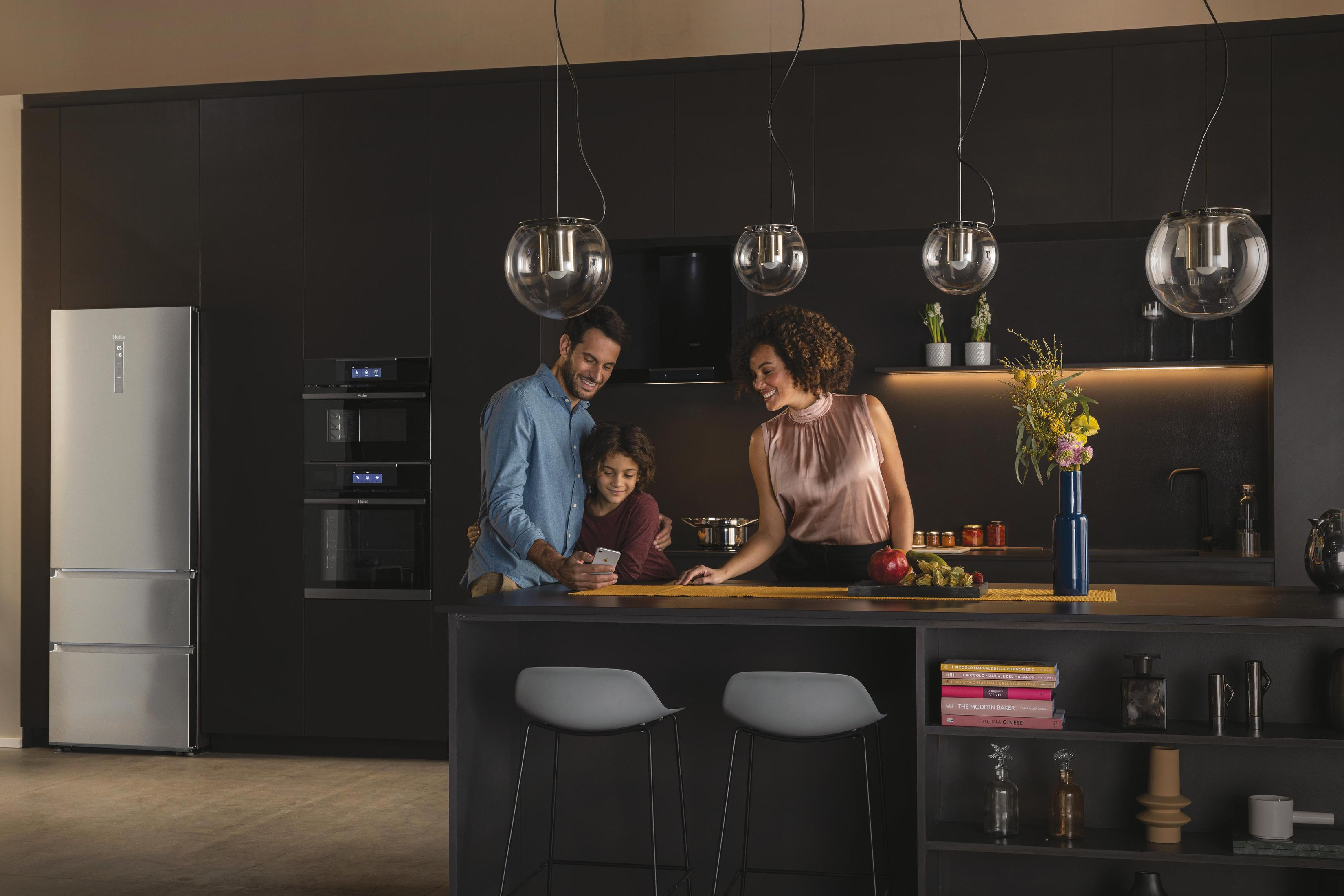 Una familia está en una cocina. Hay un refrigerador y gabinetes de cocina.