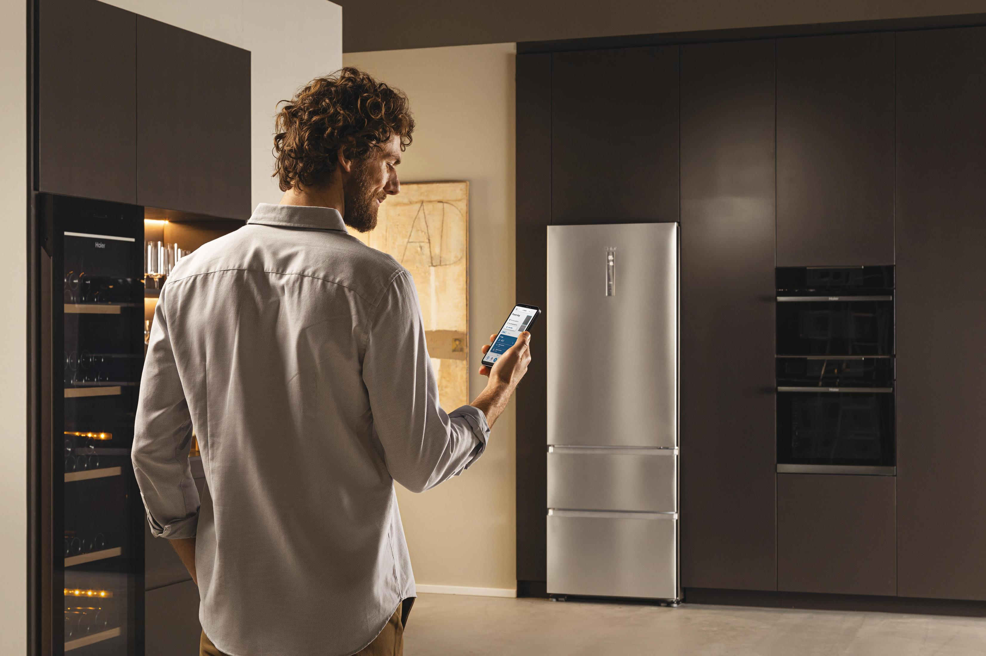 Hombre usando un teléfono en una cocina, cerca de un refrigerador.