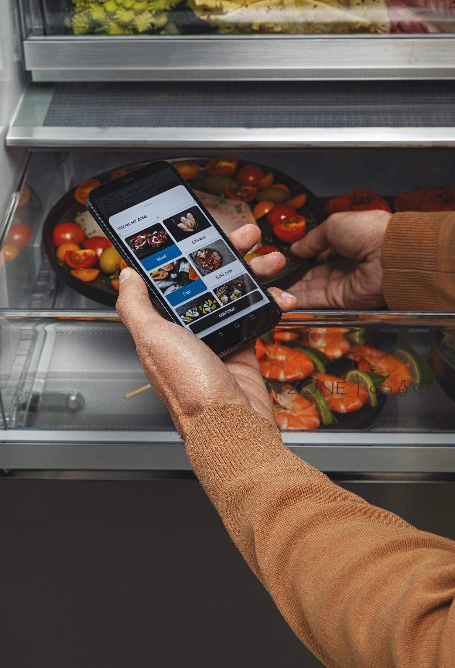 Mano sosteniendo teléfono mostrando categorías de contenido del refrigerador: carne, pescado, etc. Refrigerador abierto.
