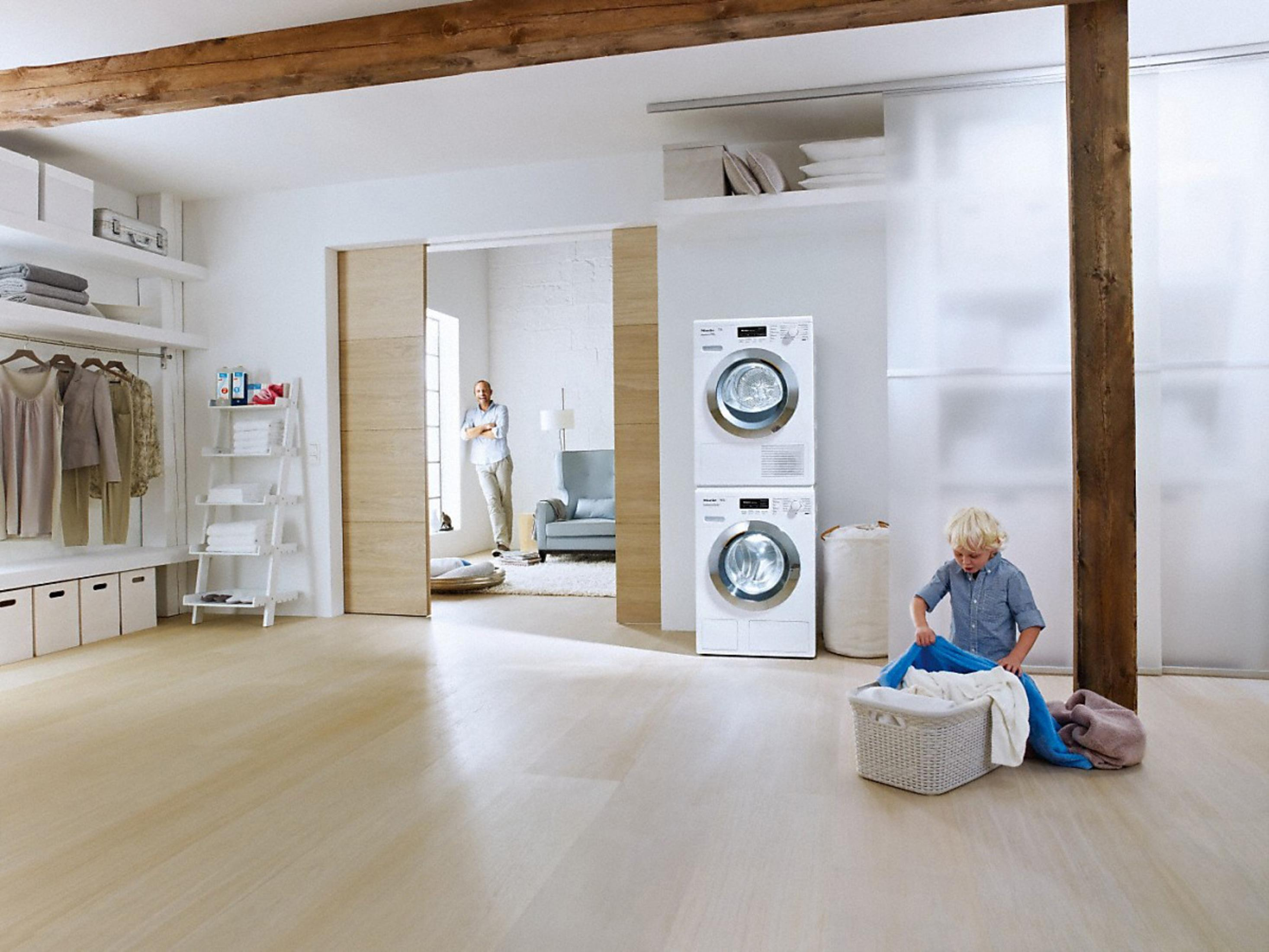 Un moderno soggiorno con pavimento in legno chiaro, zona lavanderia e un uomo in piedi.
