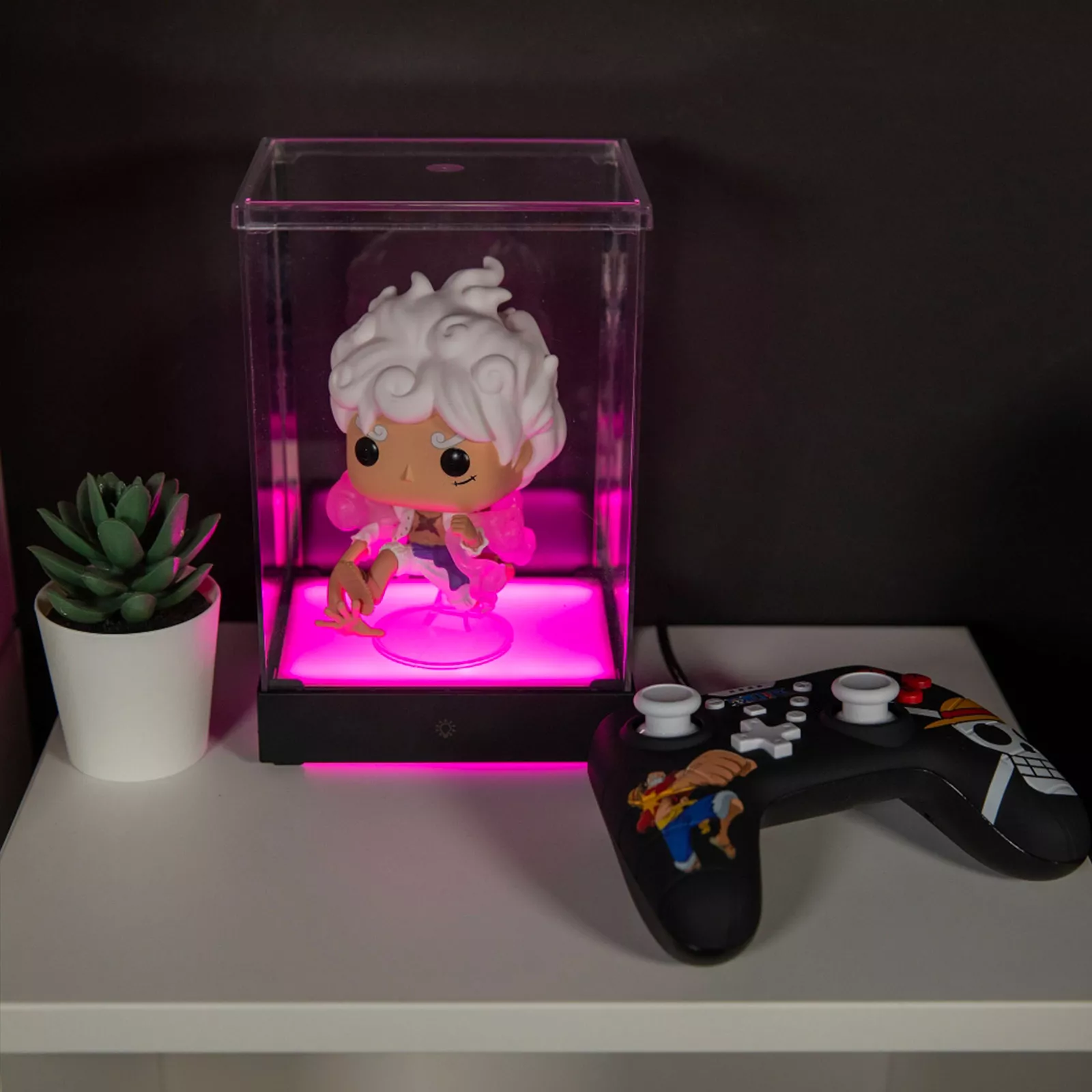 Een vitrine met een figuur erin, een kleine plant en een gamecontroller.