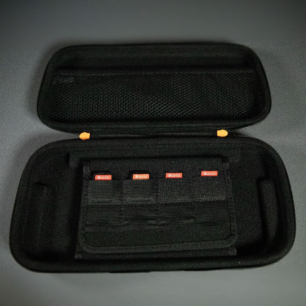 Black Switch case with orange zippers and Switch game cartridges. Dark gray surface, top view.