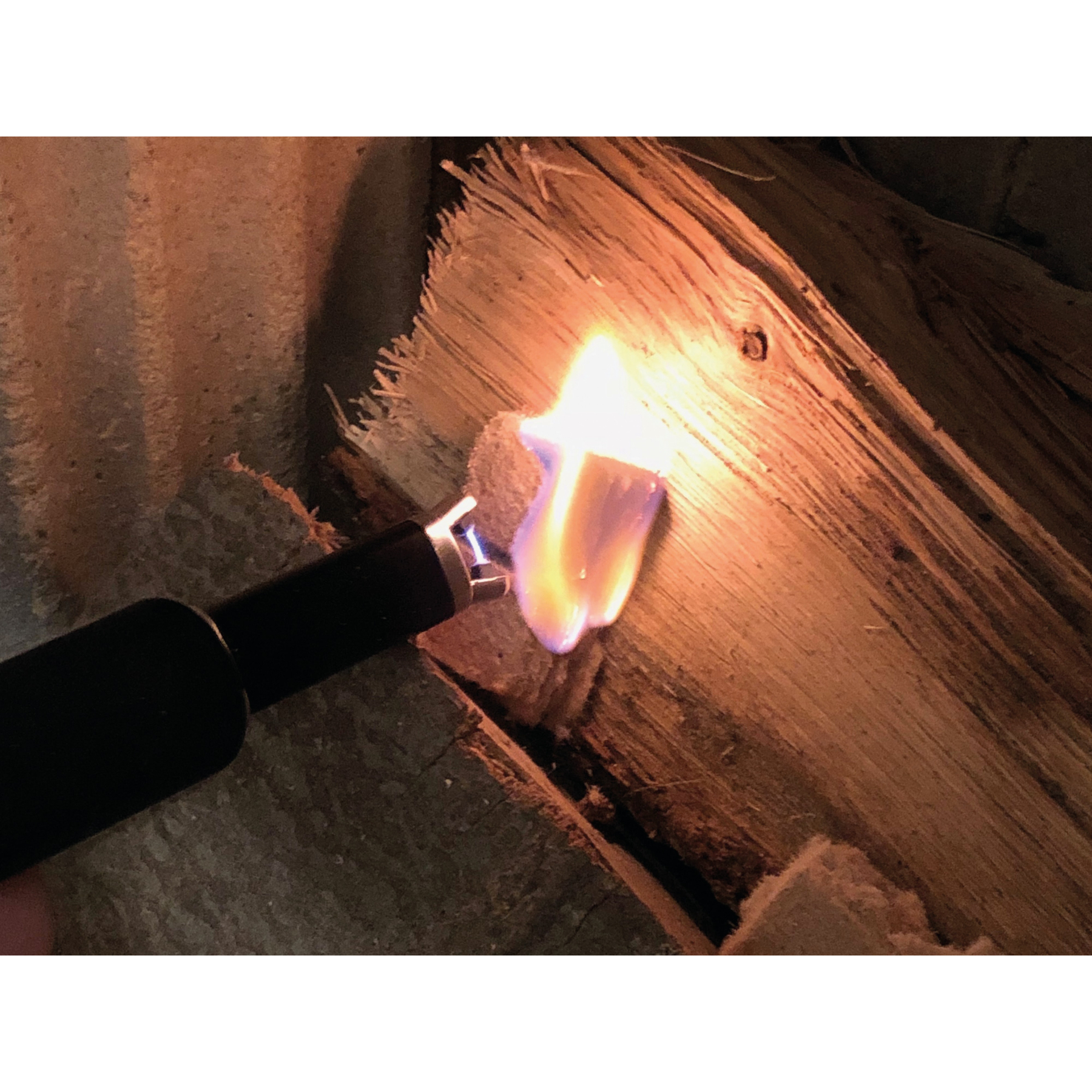 Eine Hand hält ein Feuerzeug in der Nähe von Holz und entzündet eine Flamme. Das Holz ist rau und strukturiert.