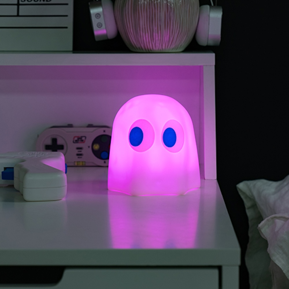 Roze spooklamp met blauwe ogen op witte tafel. Koptelefoon en andere items op de plank.