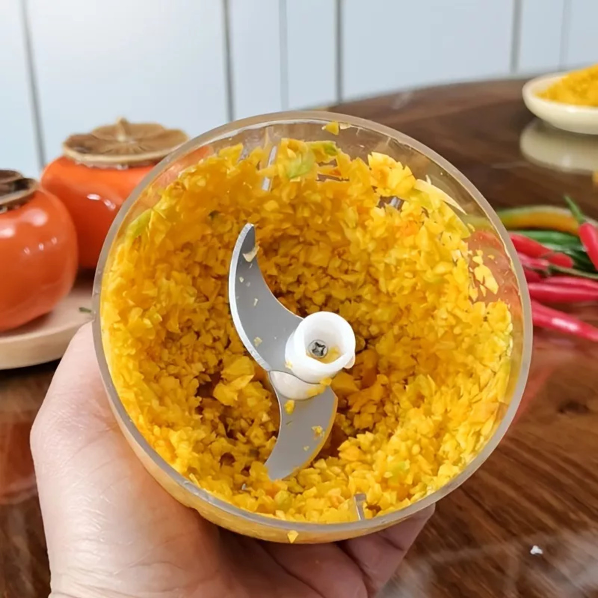 Un cuenco transparente de procesador de alimentos con ingredientes amarillos picados y una cuchilla.