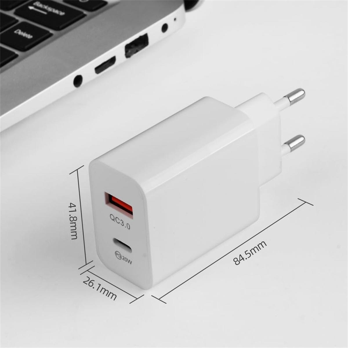 Ein weißes USB-Ladegerät mit einem roten QC3.0-Anschluss und einem 20-W-Anschluss. Abmessungen werden mit Laptop im Hintergrund angezeigt.