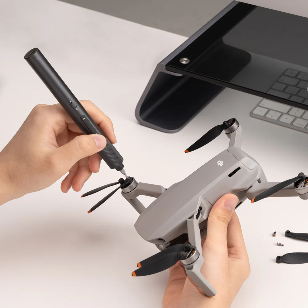Persona smonta un drone grigio con un cacciavite su una superficie bianca.