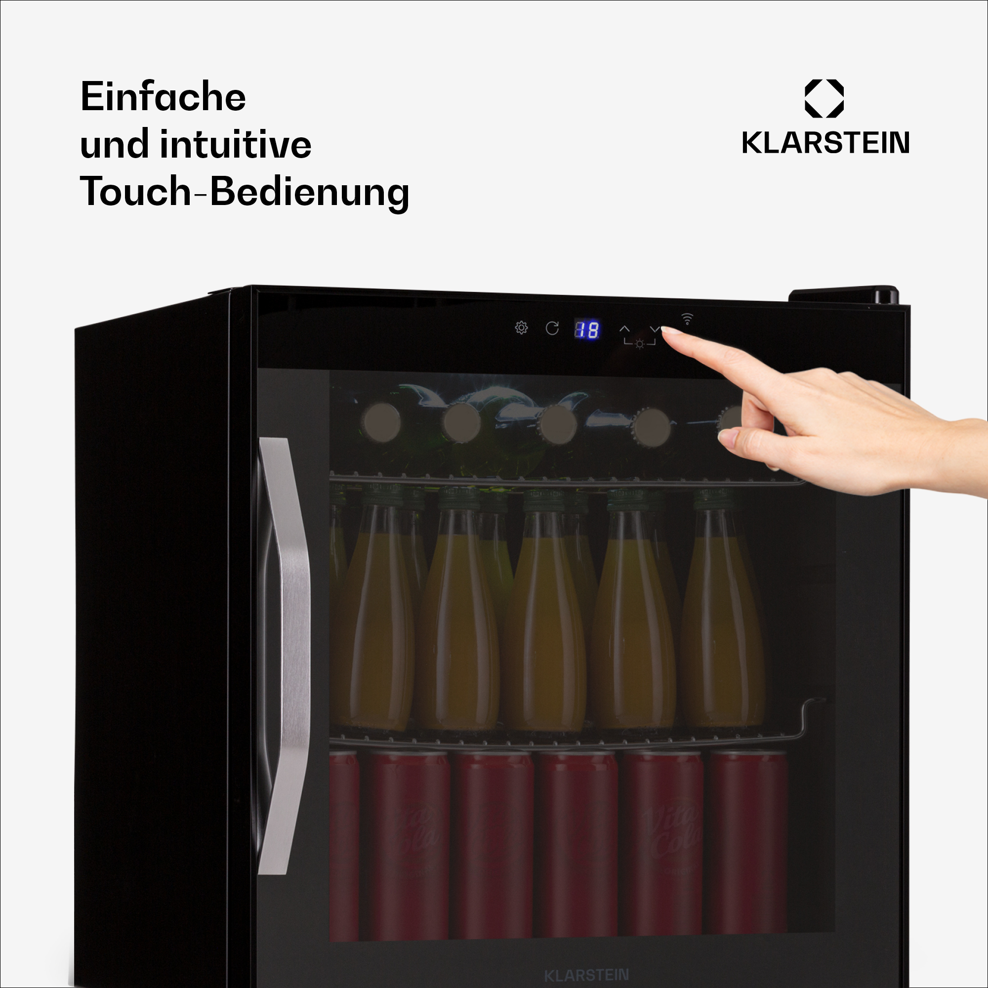 La mano di una donna che tocca un mini frigo nero con una porta a vetro, che mostra bottiglie di bevande.