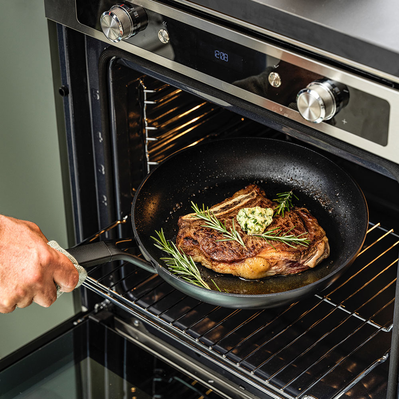 Eine Hand, die eine Pfanne mit einem Steak hält, das in einem Ofen brät.