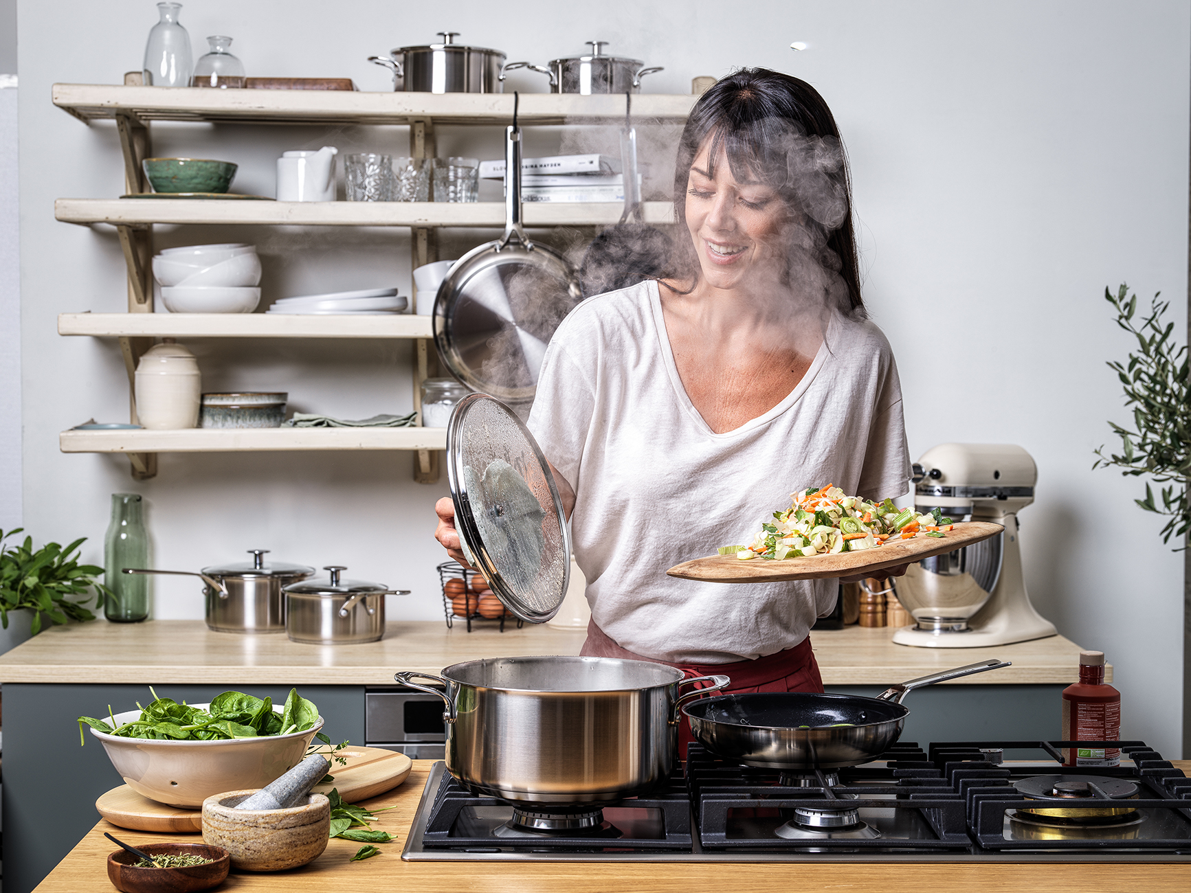 Frau kocht in einer Küche mit verschiedenen Edelstahltöpfen, Gemüse und einem KitchenAid-Mixer.