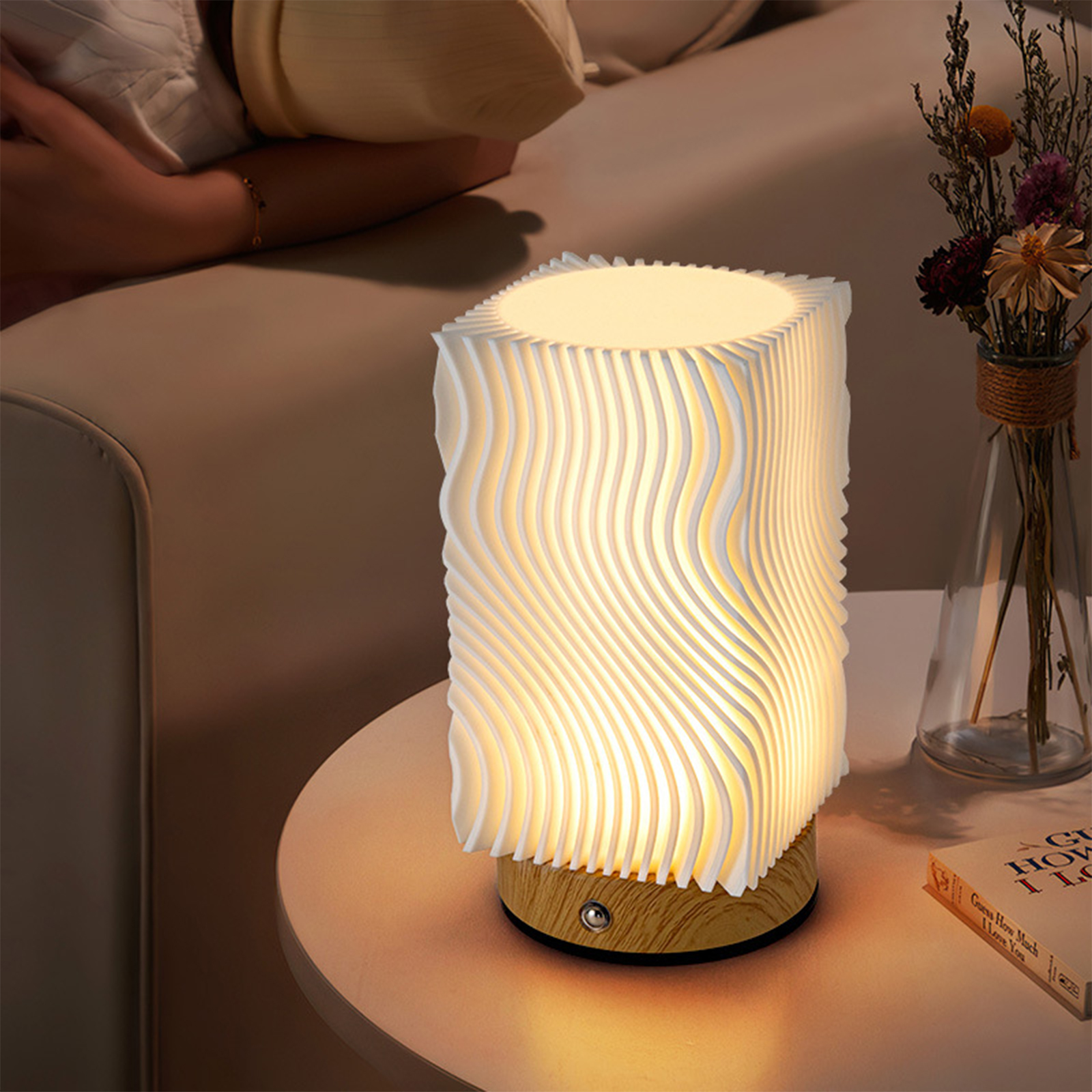 Eine moderne Lampe mit Holzsockel und wellenförmigem, weißem, papierartigem Schirm auf einem Tisch.